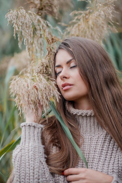 가을 공원에서 긴 머리와 갈색 눈을 가진 아름 다운 젊은 여자 팜파스 잔디 가을 근처 니트 스웨터 모델의 초상화