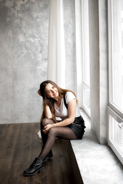 Beautiful young woman with long hair sitting on window sill in room