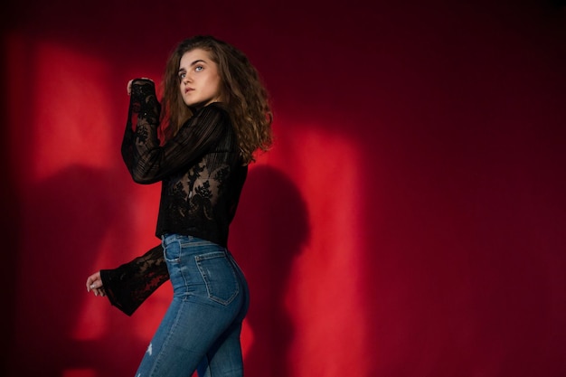 Photo beautiful young woman with makeup and curly hair dressed in a black blouse and jeans isolated red background