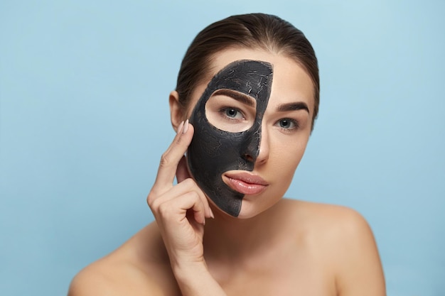 Beautiful young woman with mask for the face of black clay on\
clean fresh skin girl model beauty