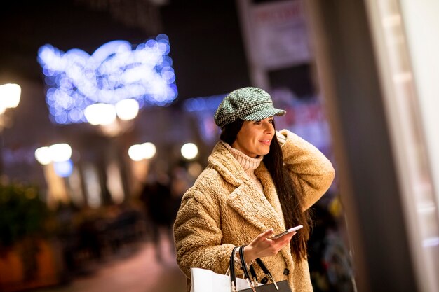 Beautiful young woman with mobile phone by the shop window at Christmas time