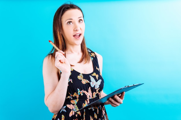 Beautiful young woman with pen and notepad pensive or doubtful on blue background