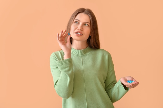 Beautiful young woman with pills on color surface