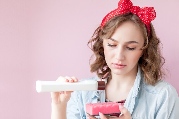 Beautiful young woman with pin-up make-up and hairstyle with cleaning tools on pink background