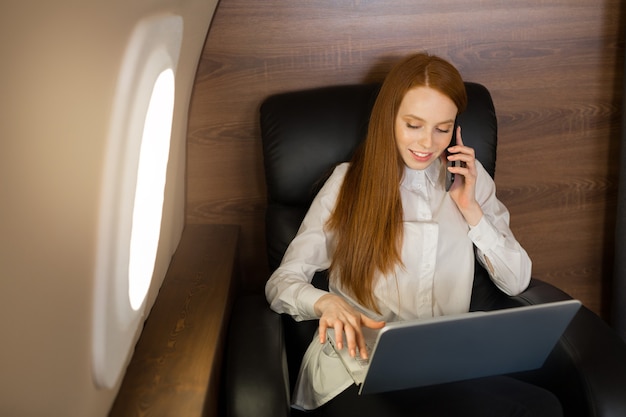 ラップトップと飛行機のキャビンで赤い髪の美しい若い女性