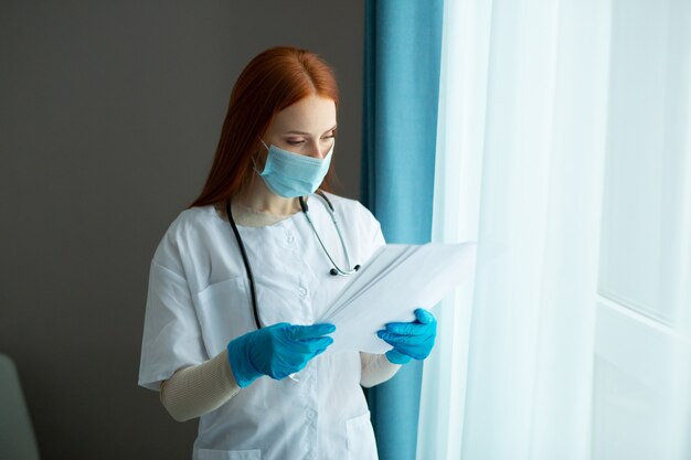 beautiful young woman with red hair in a medical gown and mask