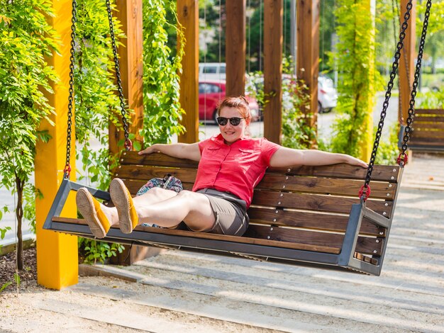 Beautiful young woman with red hair sitting on a bench in a city park, girl relaxed