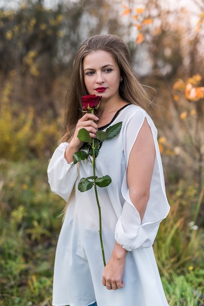 Beautiful young woman with red rose posing outdoors