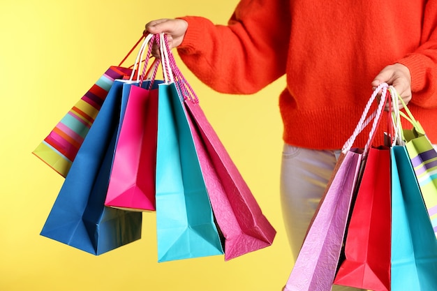 Beautiful young woman with shopping bags on color wall