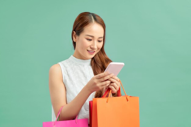 Bella giovane donna con le borse della spesa utilizzando il suo smartphone con un sorriso in piedi