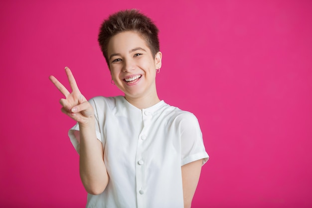 beautiful young woman with short hairdo in a white t-shirt on a pink wall