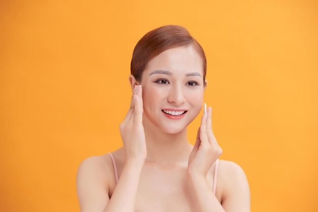 Beautiful young woman with silky skin using cotton pads on light background