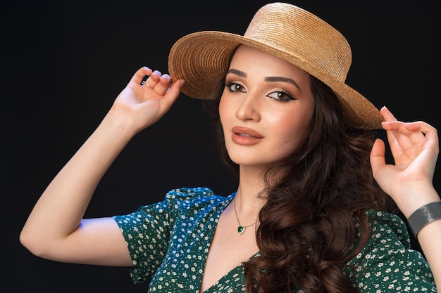 Beautiful young woman with straw hat posing against black background