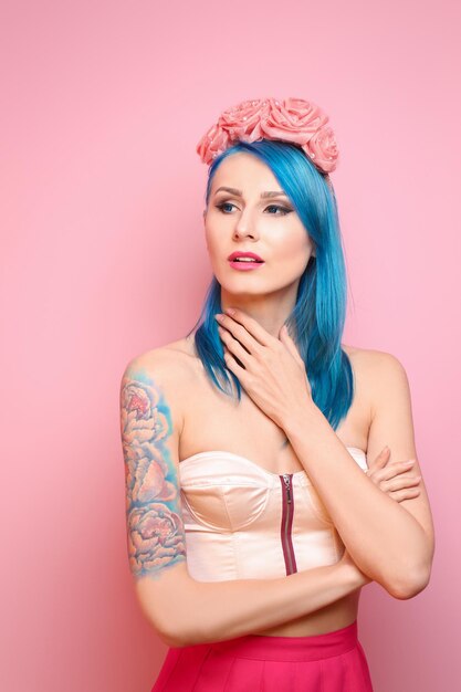 Beautiful young woman with stylish color hair and tattoo on pink background