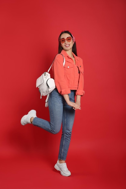 Beautiful young woman with stylish leather backpack on red background