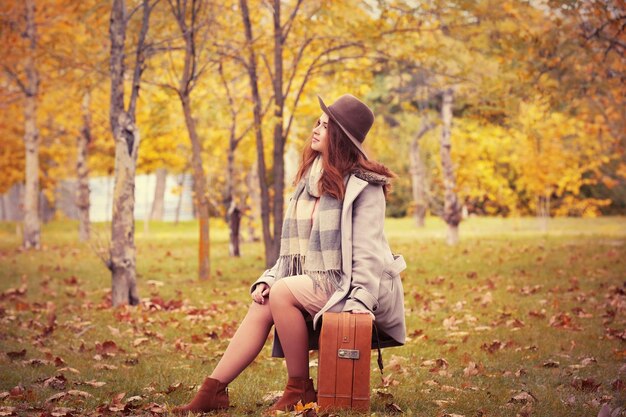 Beautiful young woman with suitcase in a autumn park