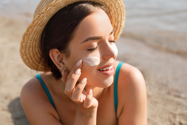 Photo beautiful young woman with sun cream on face female in hat applying moisturizing lotion on skin