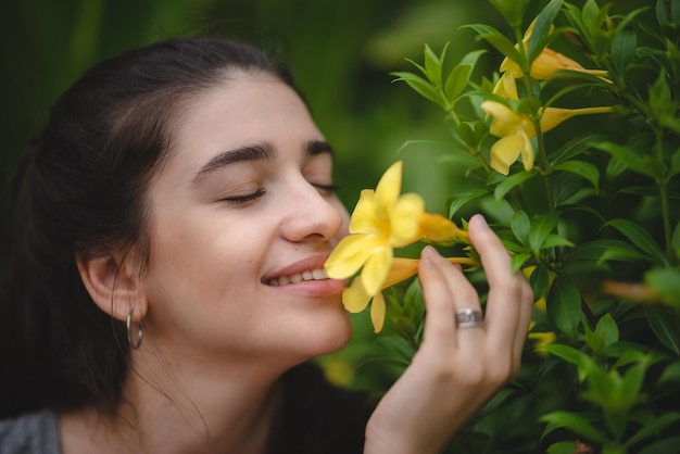 자연 속에서 즐기고 휴식을 취하는 동안 이빨 미소를 느끼고 아름다운 노란 꽃 냄새를 맡는 아름다운 젊은 여성