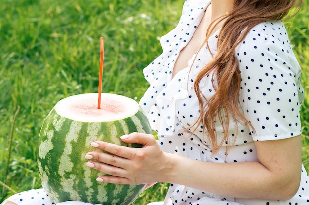 Beautiful young woman with watermelon sits on grass outdoors.