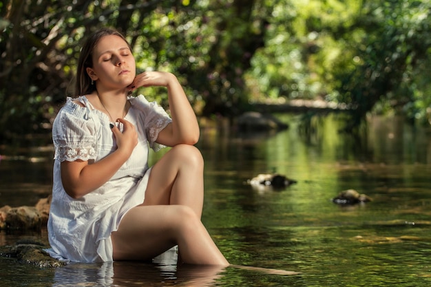 水の流れの近くに白いドレスを着た美しい若い女性。