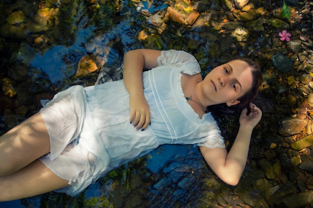 Foto bella giovane donna con abito bianco vicino al flusso d'acqua.