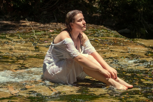 물 스트림 근처 흰 드레스와 함께 아름 다운 젊은 여자.