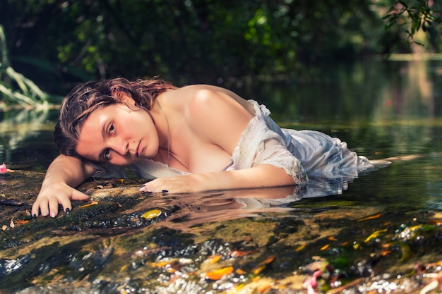 Красивая молодая женщина с белым платьем возле ручья воды.