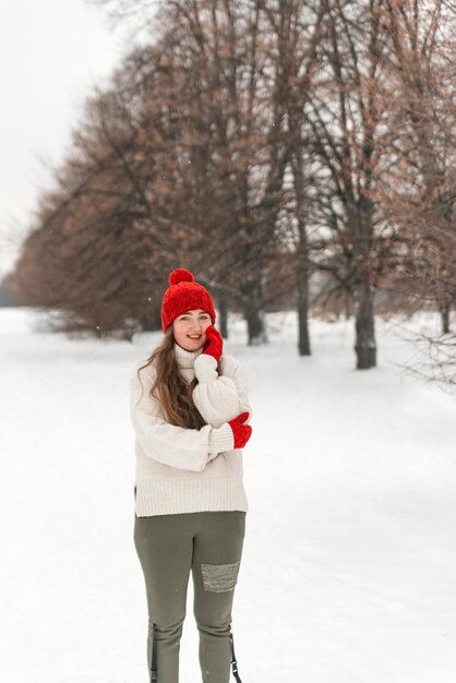 Beautiful young woman in woolen hat outdoors cold weather Young woman in knitted red hat and mittens winter park Vertical frame