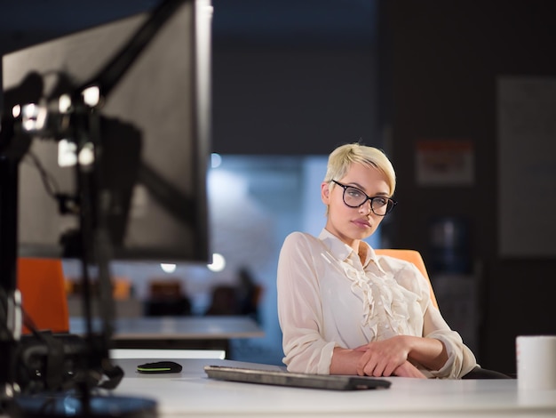 Beautiful young woman working on computer at night in dark
office. the designer works in the later time.