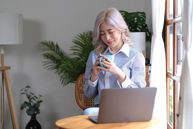 거실에 앉아 커피를 마시며 노트북 컴퓨터 작업을 하는 아름다운 젊은 여성