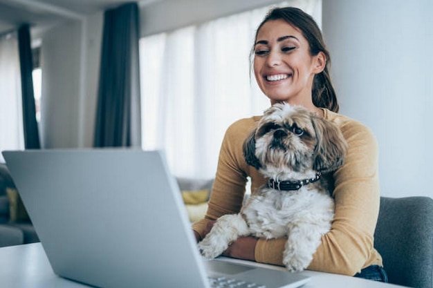 beautiful young woman working on laptop while her dog sits in her lap young woman
