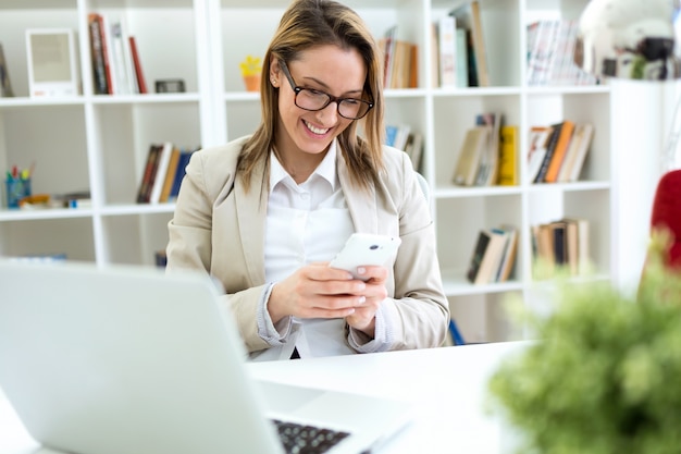 Beautiful young woman working with mobile phone in her office.