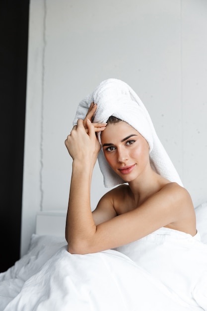 Beautiful young woman wrapped in bath towel sitting in bed