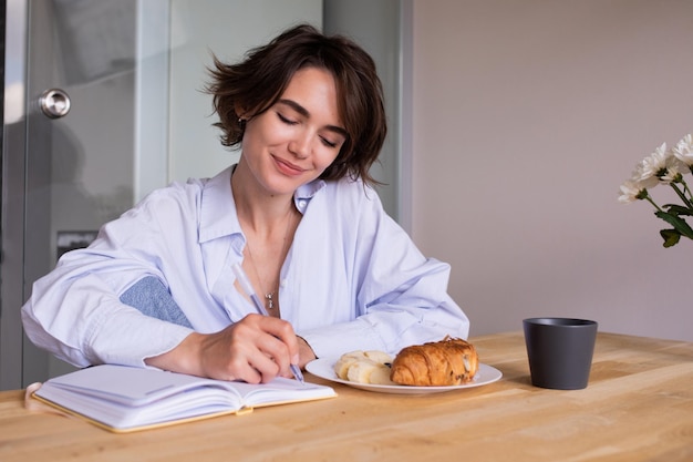 Beautiful young woman writing at notebook in home