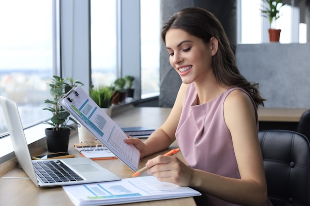 Beautiful young woman writing something down while sitting in modern office.