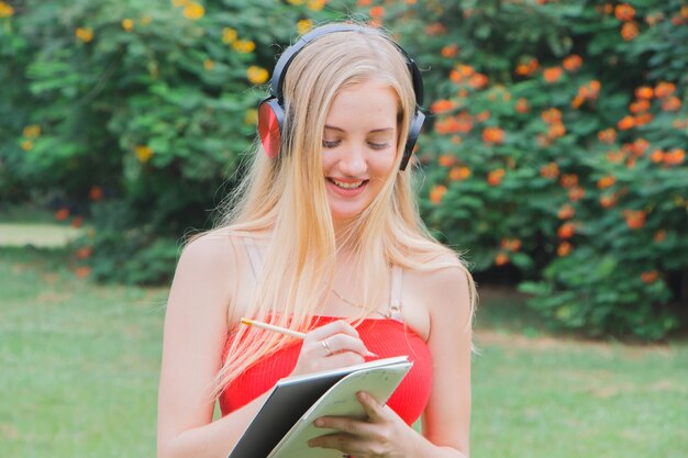 Beautiful young woman writing with note at park