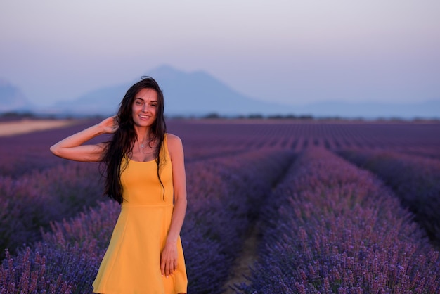 紫の花のラベンダー畑でリラックスして楽しんでいる黄色のドレスを着た美しい若い女性