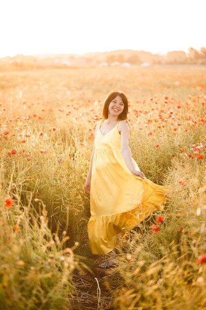 여름날 양귀비 밭을 걷고 있는 노란 드레스를 입은 아름다운 젊은 여성. 시골에서 꽃을 즐기는 소녀. 선택적 초점