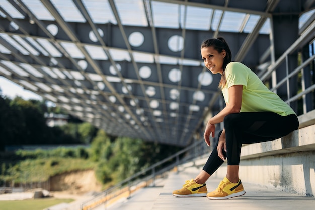 Beautiful young woman in yellow t-shirt, black leggings and sport sneakers sitting.
