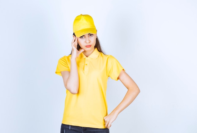 노란색 티셔츠와 모자를 쓴 아름다운 젊은 여성이 흰색 배경에 포즈를 취하고 있습니다.