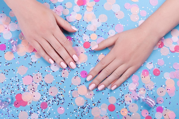 Beautiful young womans hands on blue pastel background with festive multi color confetti