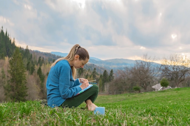 Beautiful young women works remotely in nature in the mountains