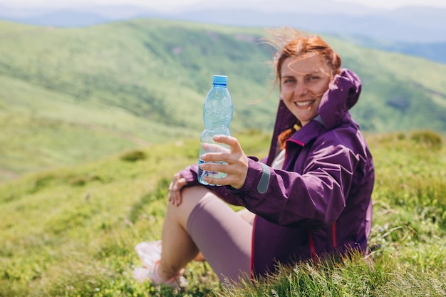 사진 beautifull 여성 관광객은 높은 봉우리에서 물을 마십니다. 놀라운 전망 자유 행복 여행 및 휴가 개념 산에 있는 플라스틱 병에 순수한 식수 한 병