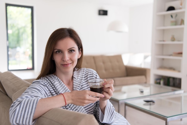 彼女の豪華な家の別荘で朝のコーヒーを楽しんでいるバスローブを着た美しい若い女性