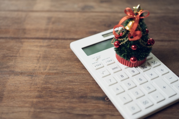 A beautifully decorated Christmas tree placed on a white calculator and with a miniature book. 