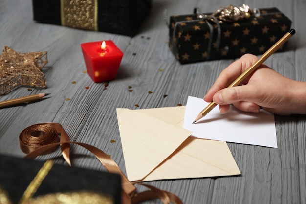 Beautifully decorated gift boxes and woman signing greeting card on wooden background