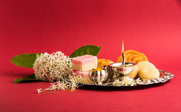 Красиво оформленная пуджа Тали для празднования Дивали для поклонения, с индийскими сладостями, порошком хульди или куркумы и кумкумом на красной поверхности