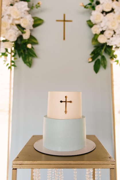 Beautifully decorated white and blue cake for the sacrament of the baptism of a boy on the background of a stylish photo zone