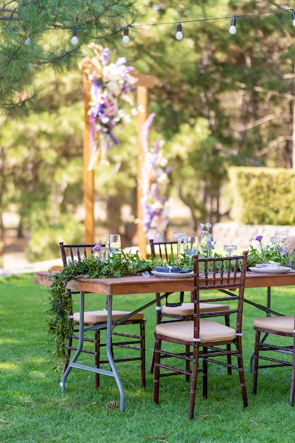 Beautifully decorated wooden table in a summer open-air cafe. Green branch and fresh flowers table decoration