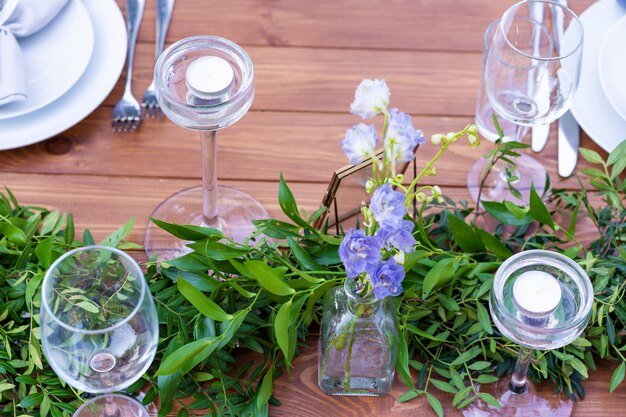 Beautifully decorated wooden table in a summer open-air cafe. Green branch and fresh flowers table decoration.